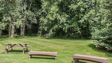 Un espacio con césped, tres bancos de madera y una mesa de picnic.