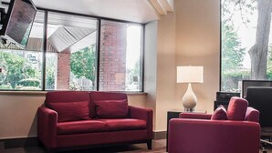 A modern hotel room with a red sofa, a lamp, and large windows offering a view of the outdoors.