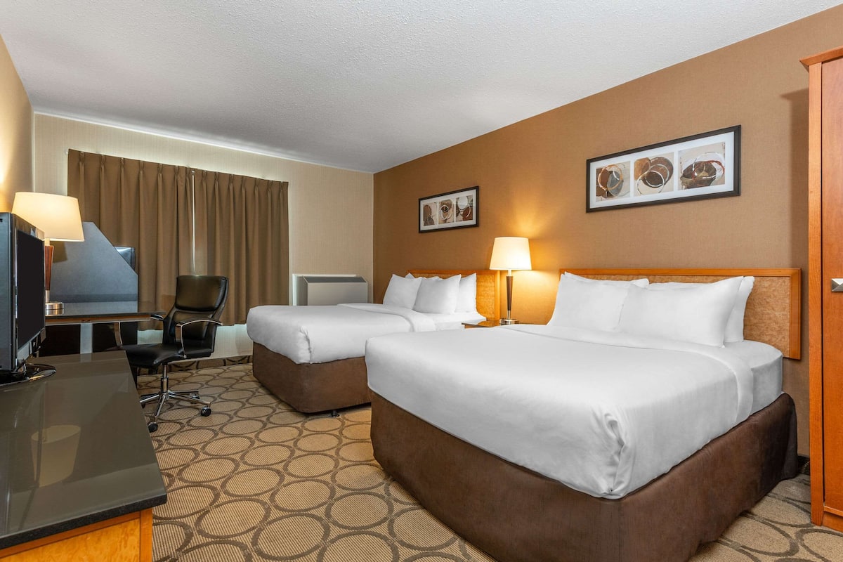 A hotel room with two beds, a desk, a TV, and a chair.