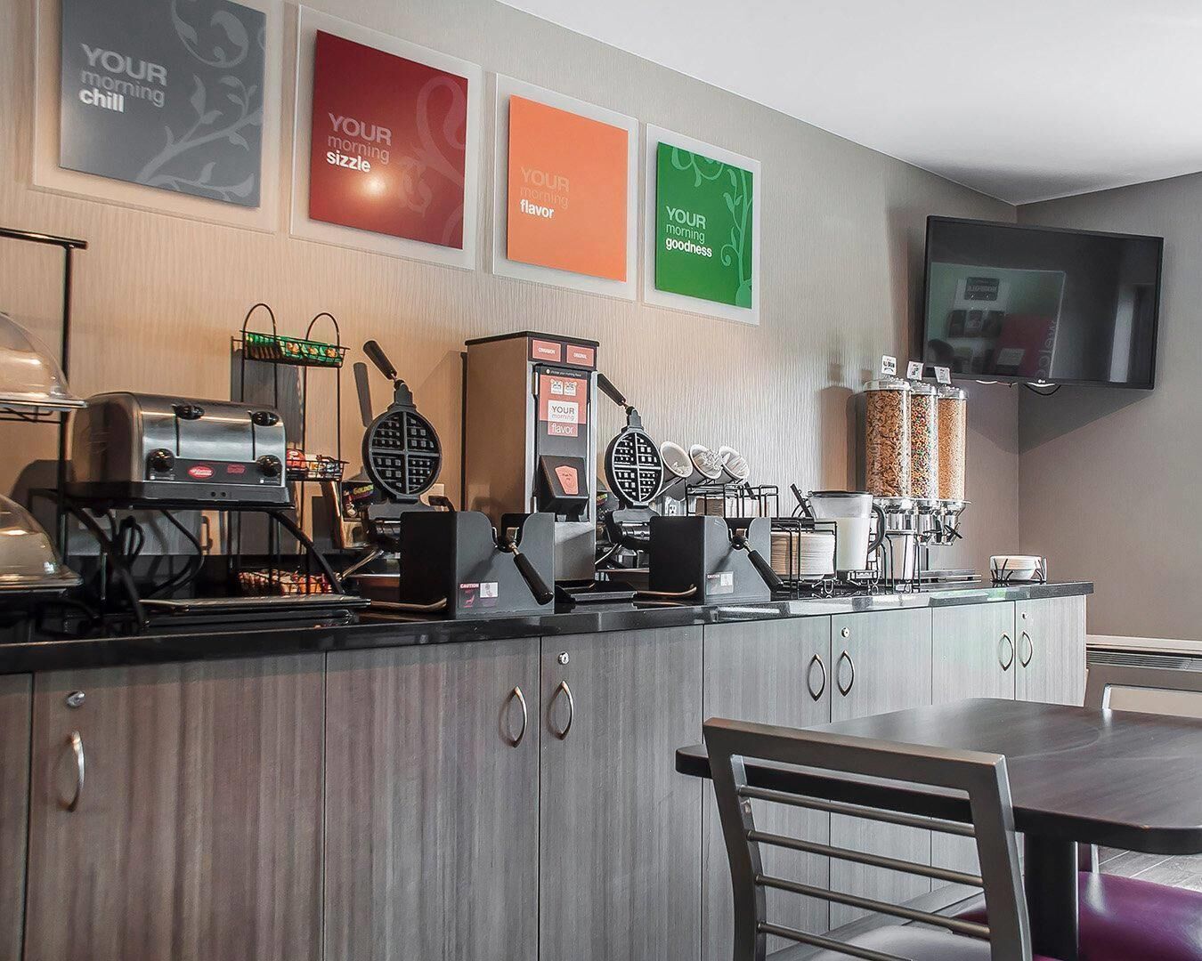 A breakfast bar with waffle makers, a coffee machine, and a TV mounted on the wall.