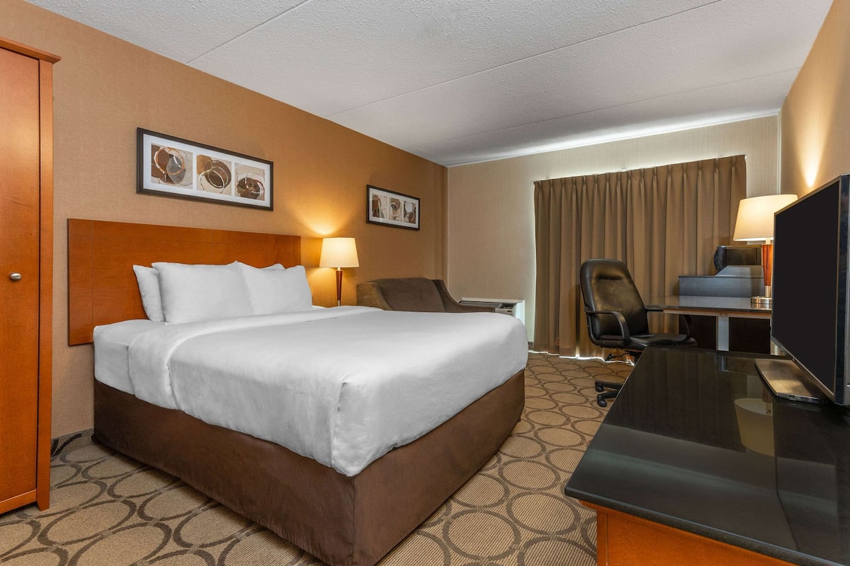 A hotel room with a large bed, a desk with a flat-screen TV, a chair, and two wall-mounted lamps.