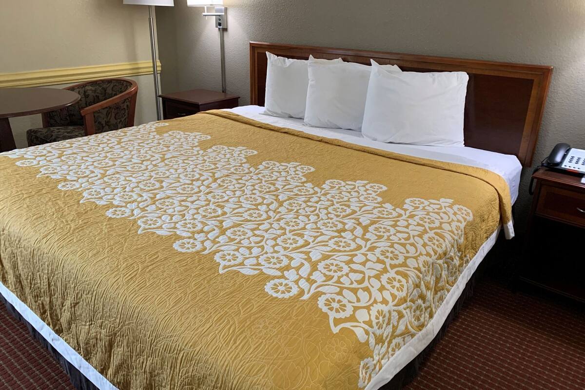 A hotel room with a bed, a bedside table with a phone, a lamp, and a chair.