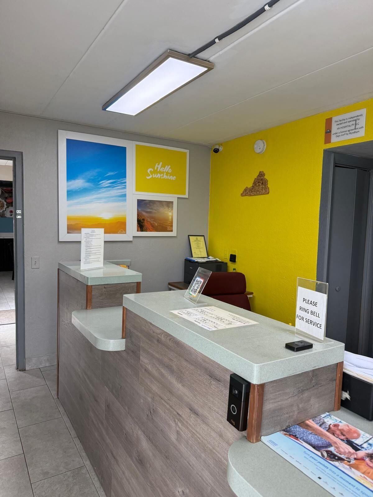 Mostrador de recepción con un cartel que indica la disponibilidad de servicio, una obra de arte enmarcada y una pared de color amarillo brillante.