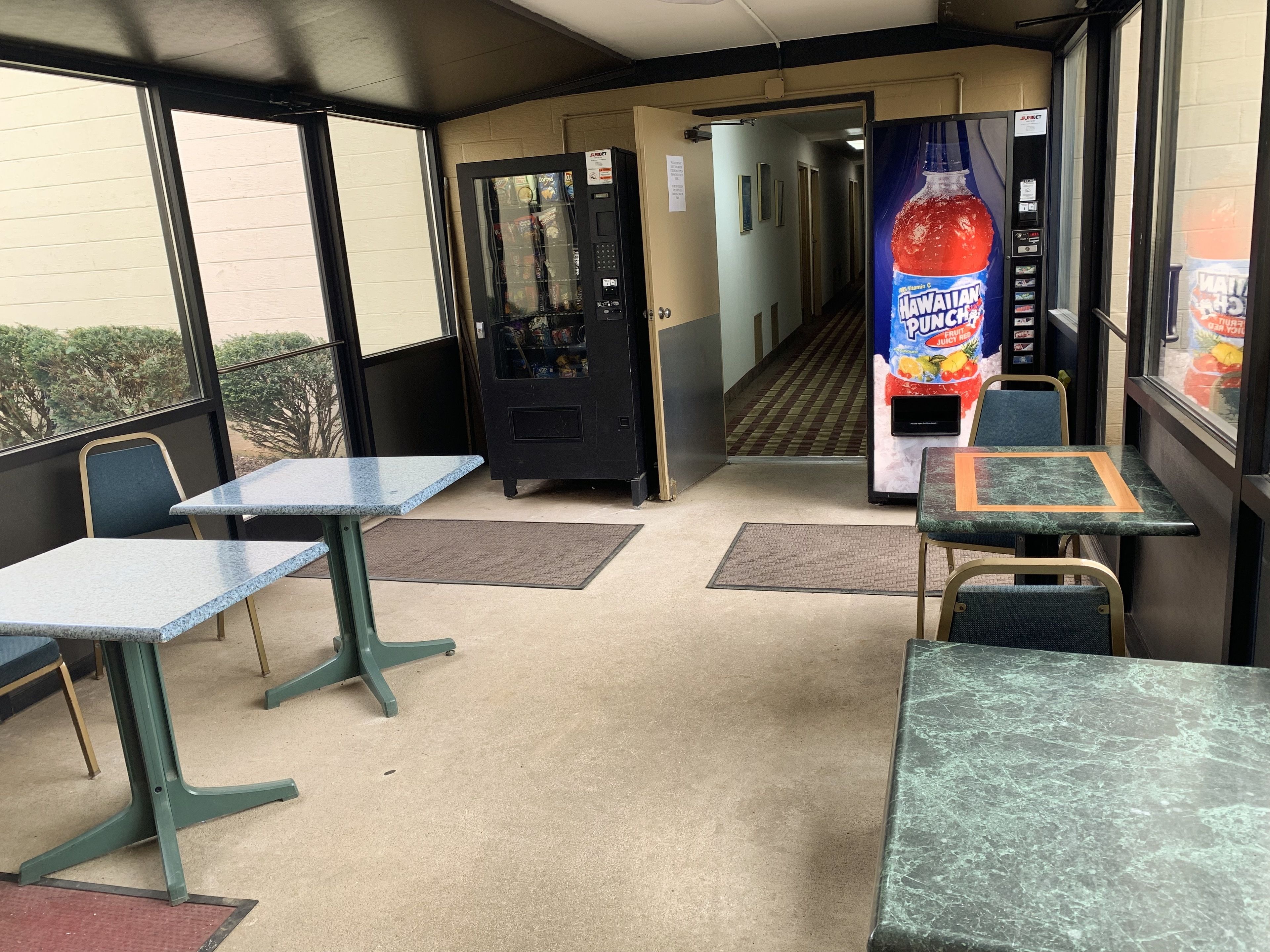 A seating area with tables and chairs, vending machines, and a hallway leading to another room.