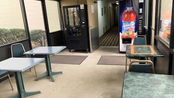 A seating area with tables and chairs, vending machines, and a hallway leading to another room.