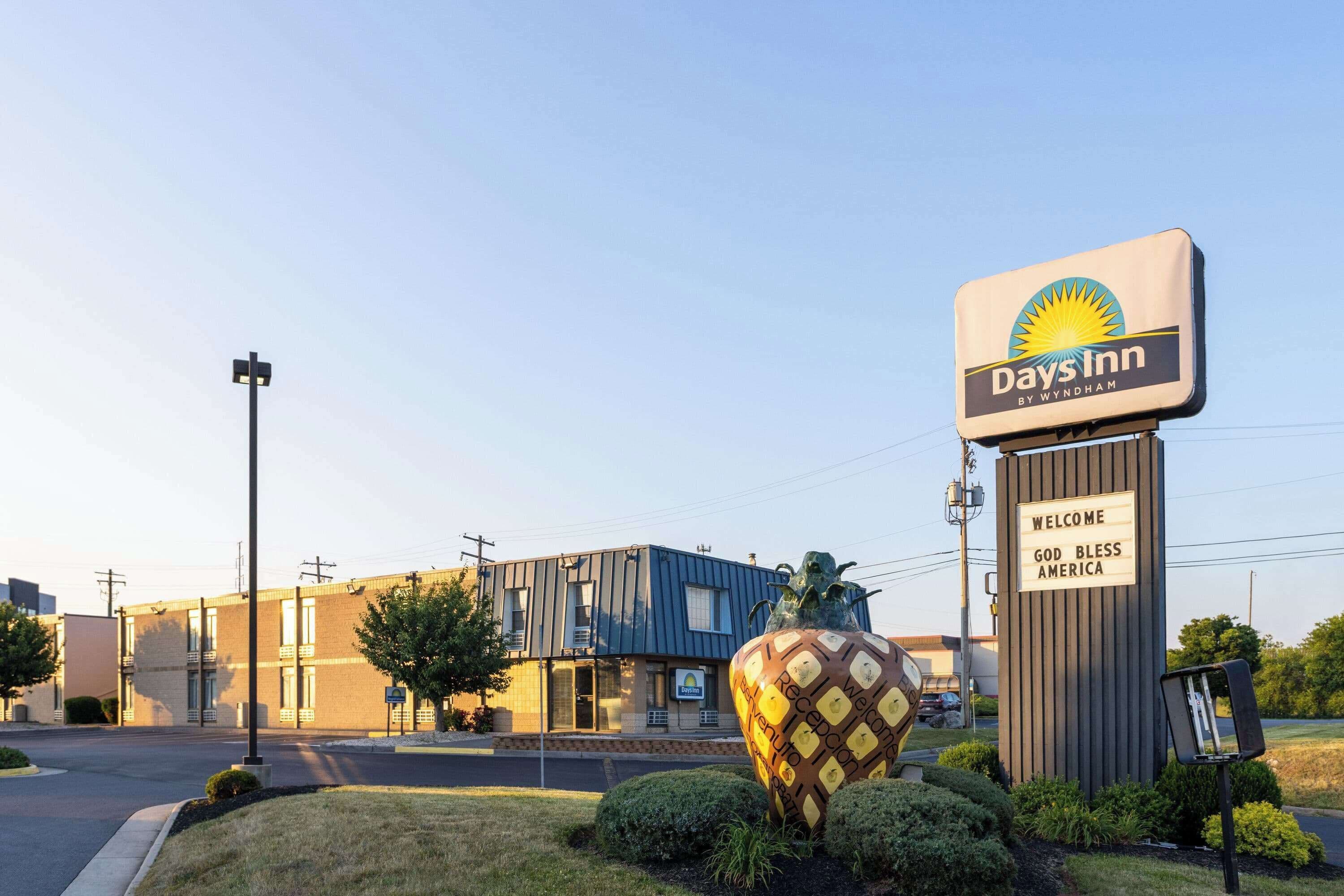 Une enseigne Days Inn avec un message d’accueil, un grand pot décoratif en forme de fraise et un bâtiment au design moderne.