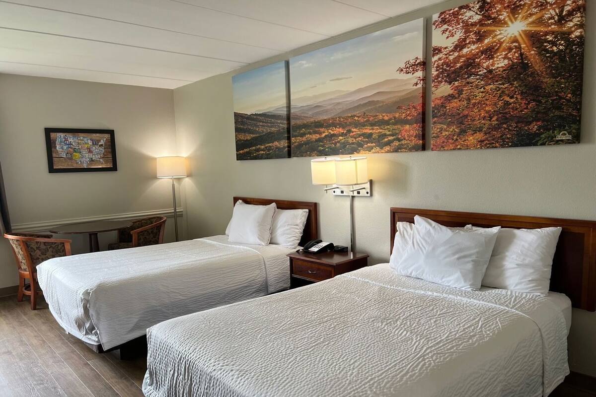 A hotel room with two beds, a desk, and a chair. There are two wall-mounted lamps and a framed picture on the wall.