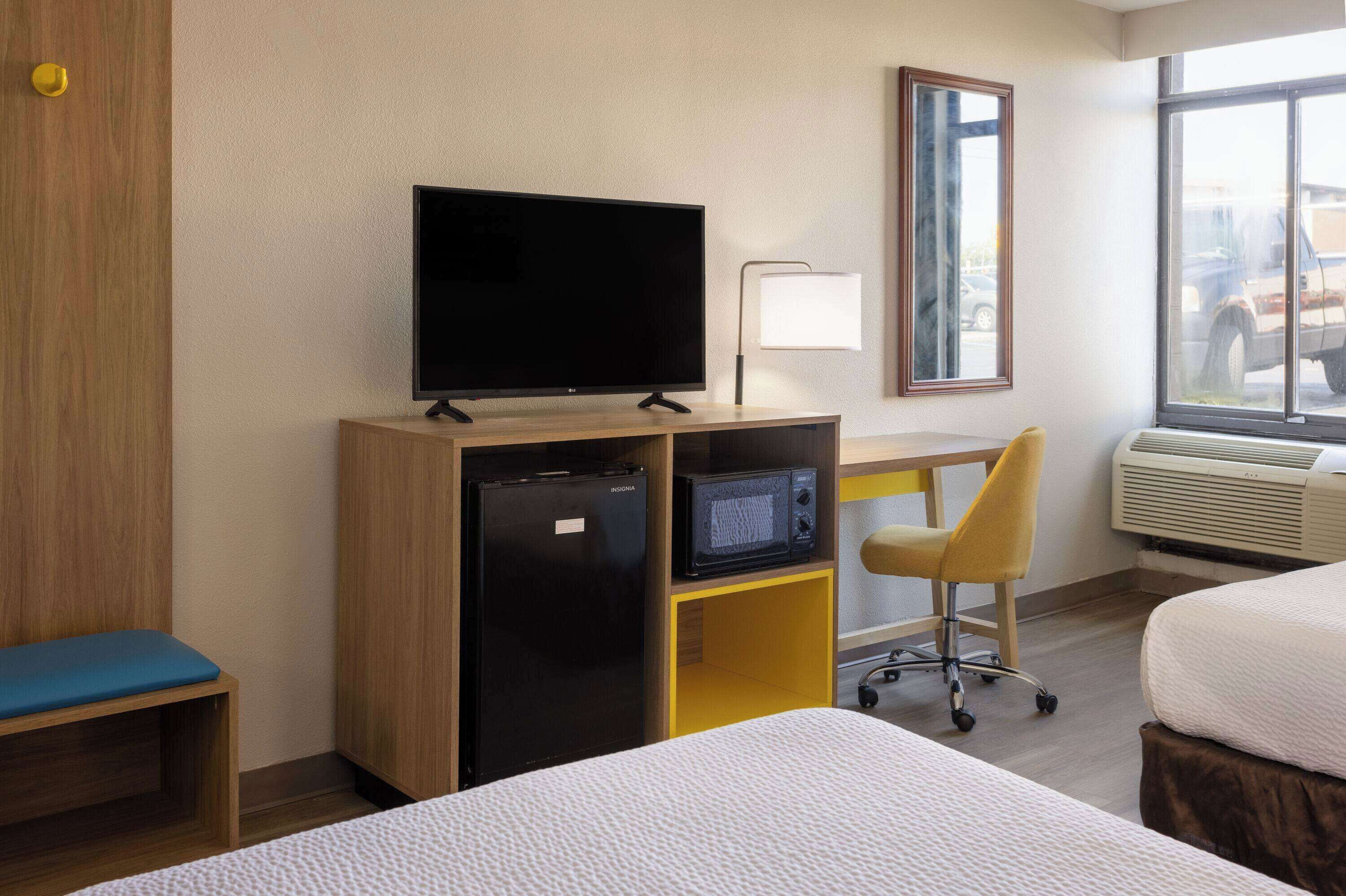 Hotelkamer met een bed, een bureau met stoel, een televisie, een koelkast, een magnetron en een raam met uitzicht.