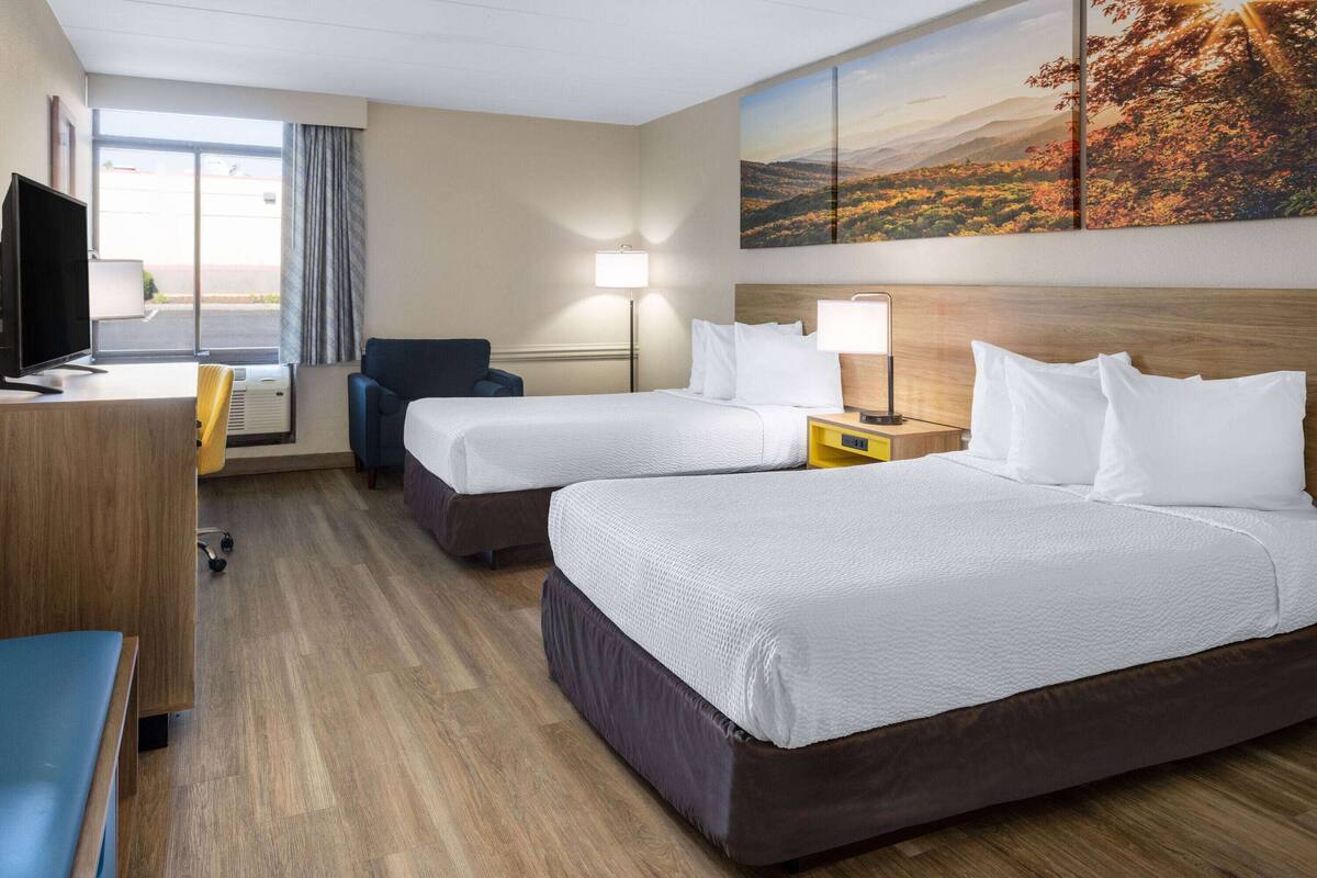 A hotel room with two beds, a desk with a computer, a chair, and a painting of a landscape.