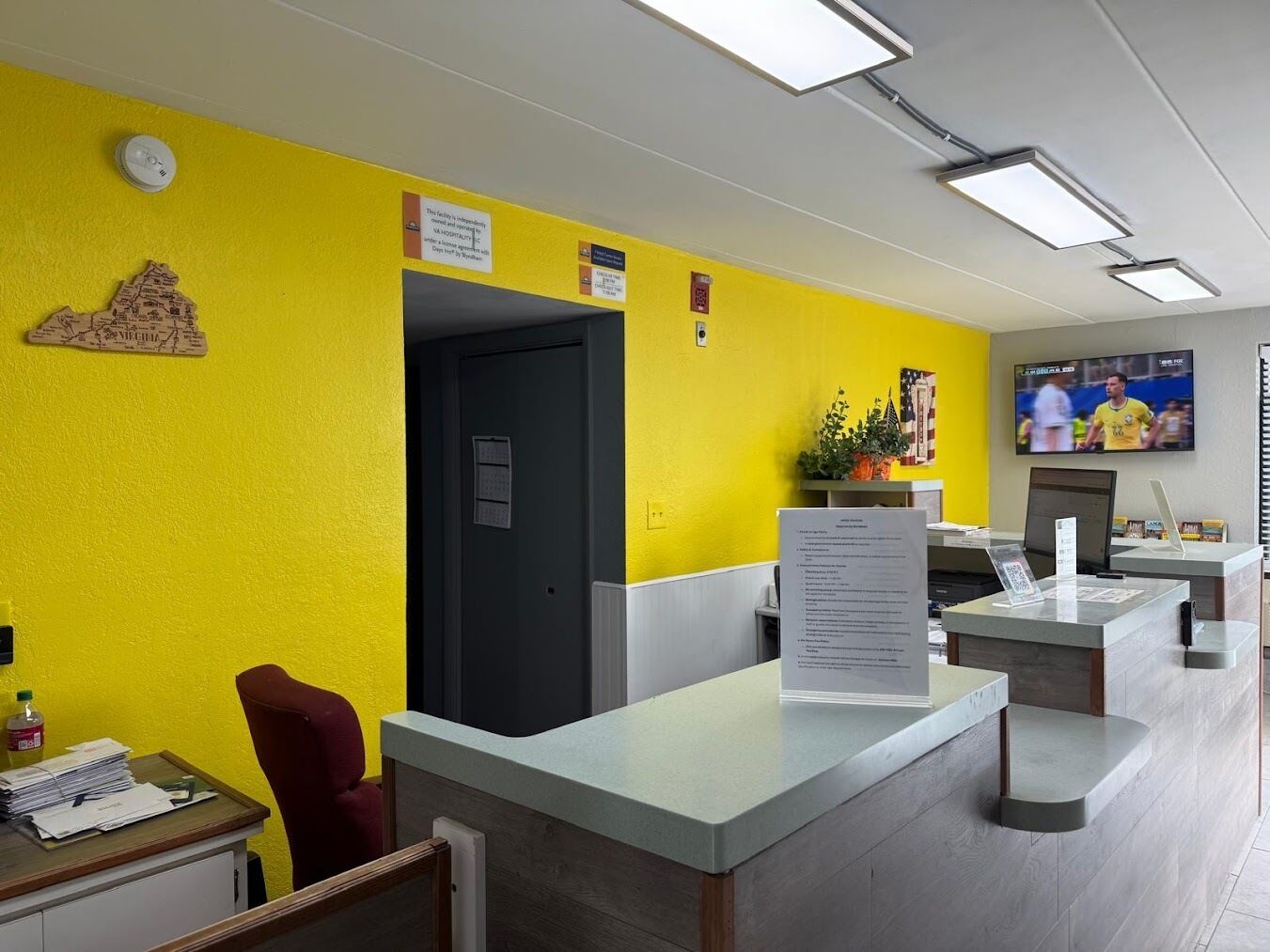A reception area with a bright yellow wall, a black door, and a reception desk with a menu sign.