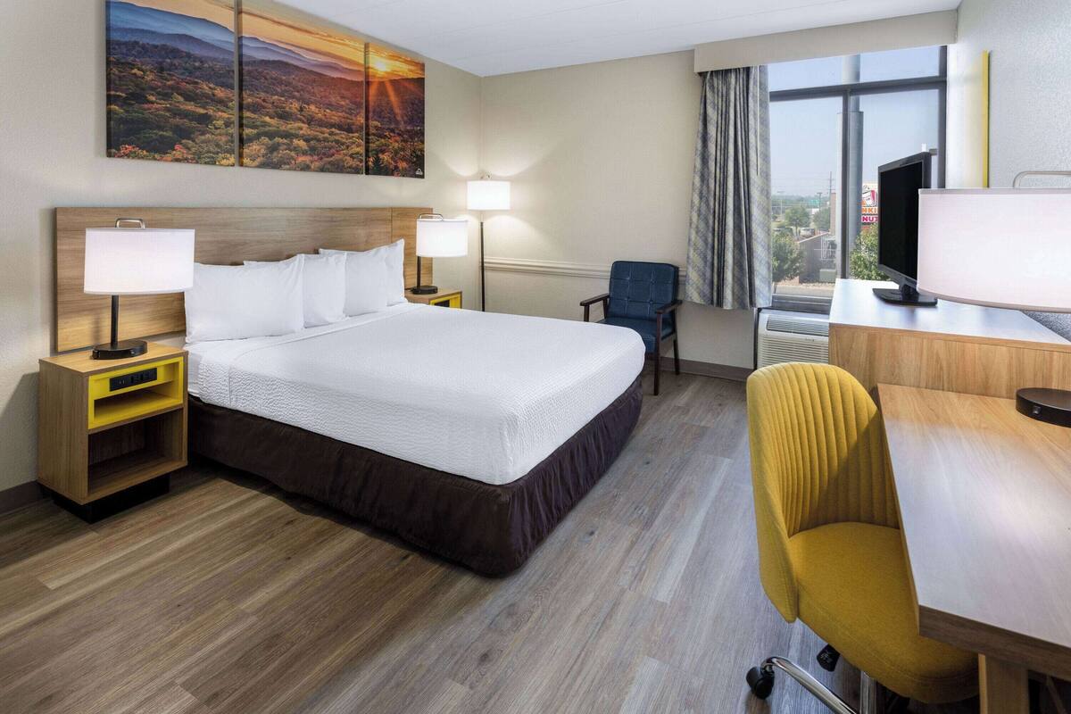A hotel room with a large bed, two bedside tables with lamps, a desk with a chair, and a television.