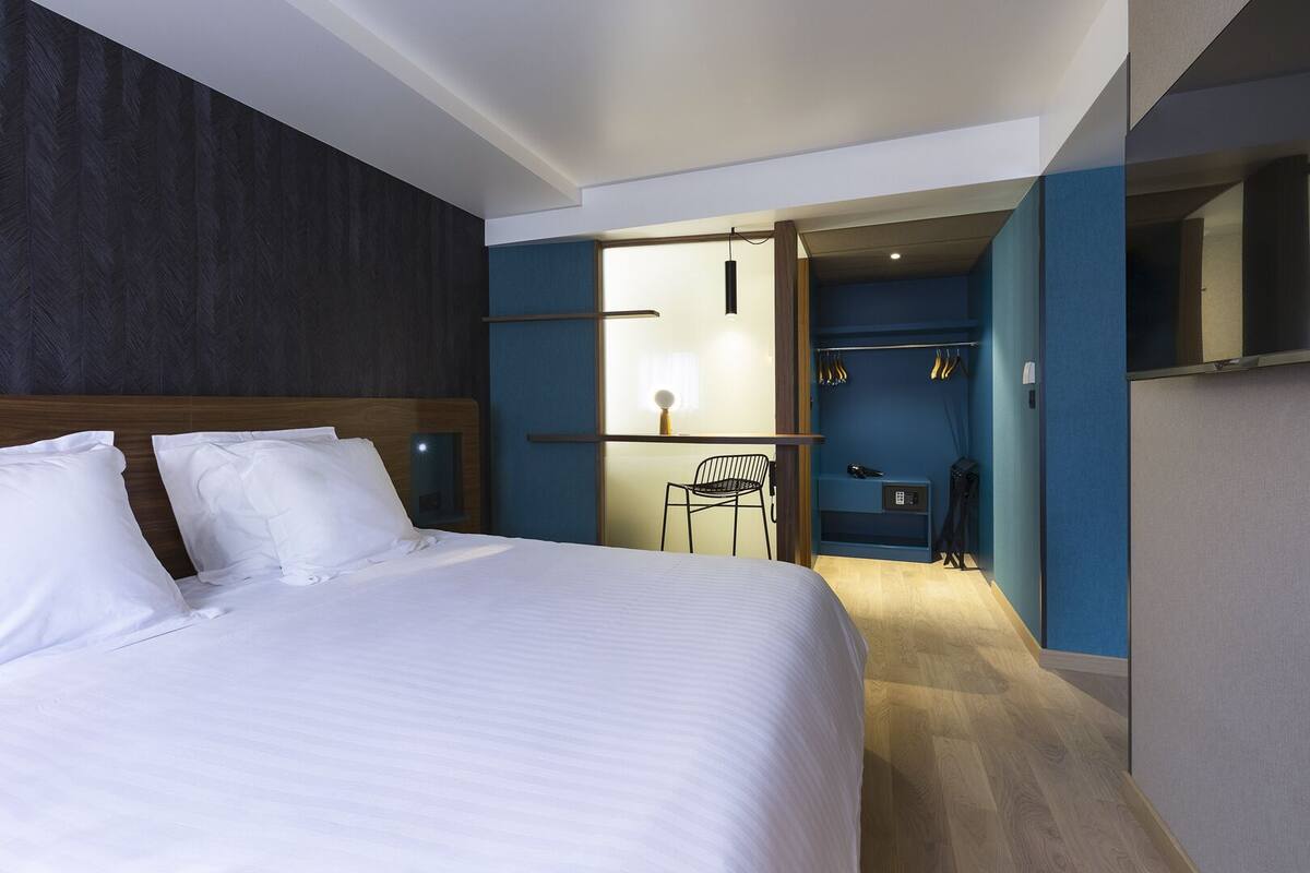 Una habitación de hotel moderna con una cama grande, un escritorio con una silla y un vestidor.