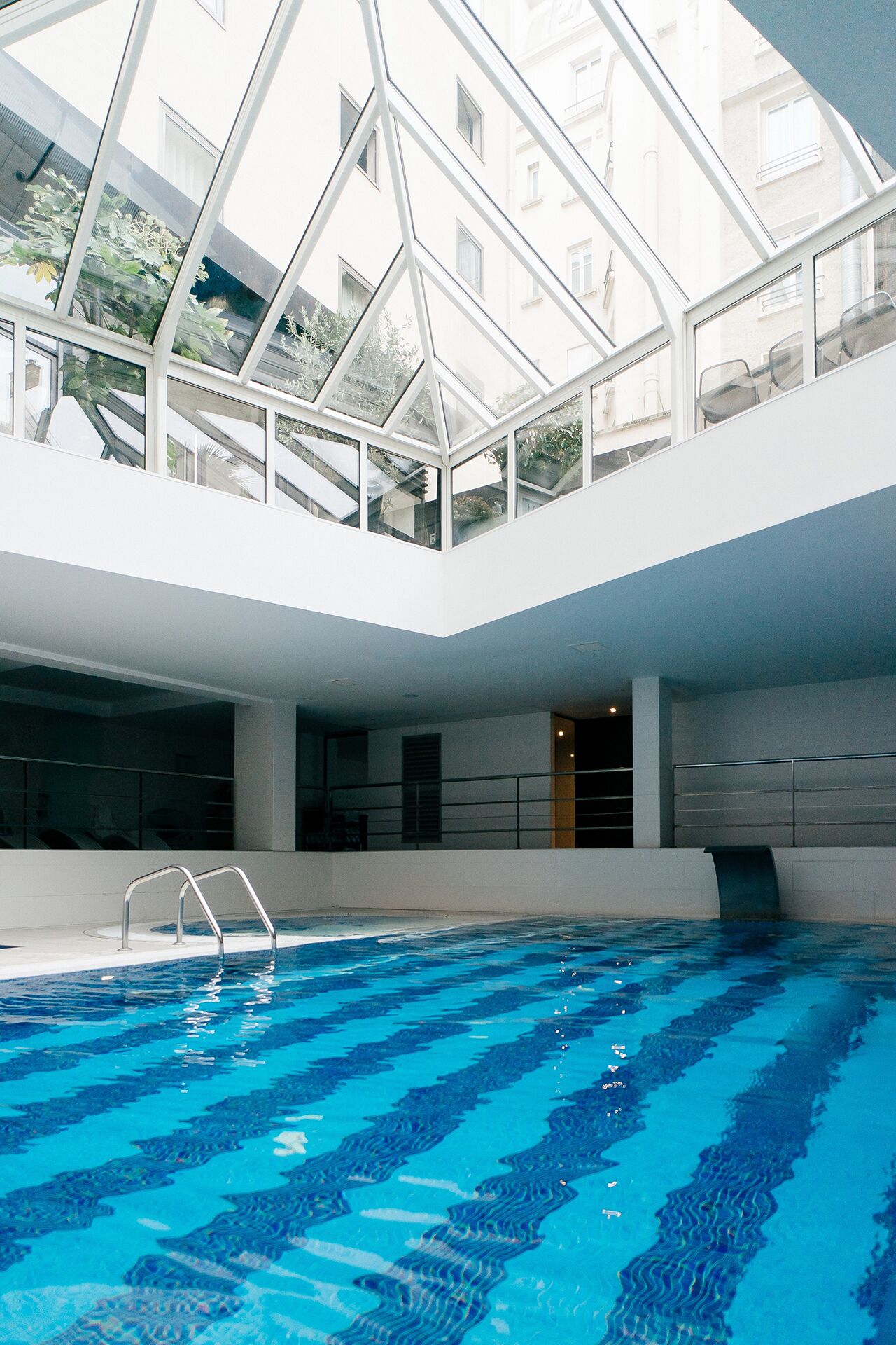Une piscine intérieure dotée d’un toit en verre, d’une eau d’un bleu cristallin et d’une architecture moderne.