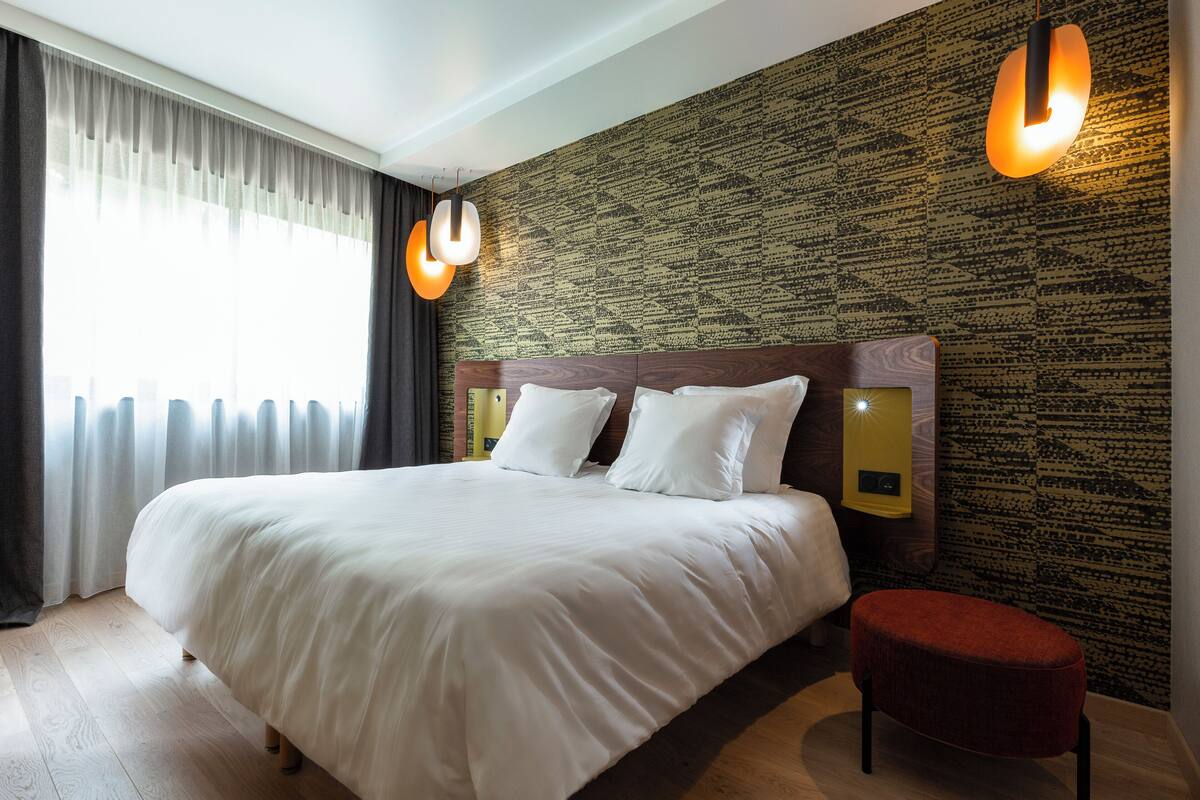 Une chambre d’hôtel avec un grand lit, un pouf rouge et un mur orné d’un motif.