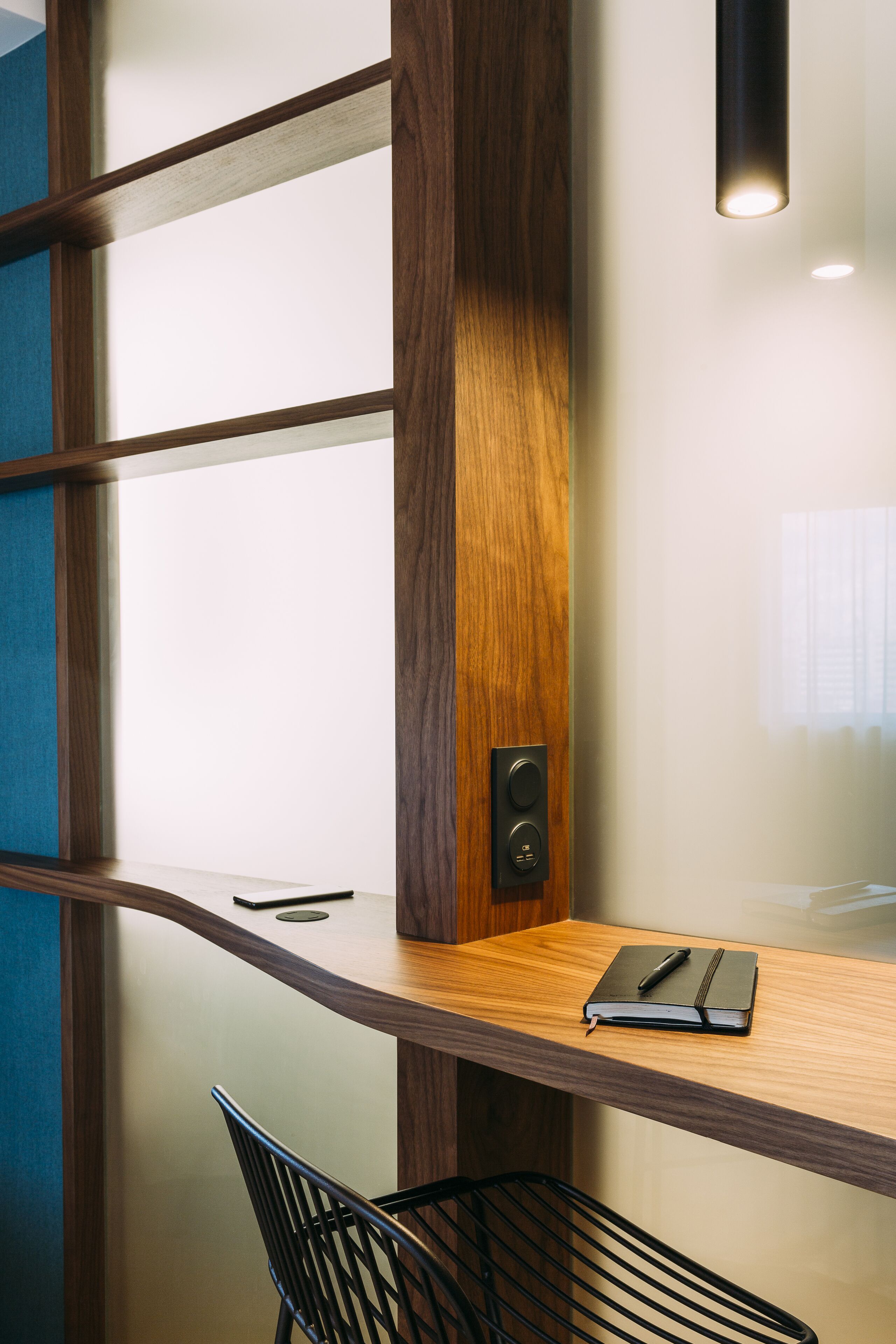 Un bureau moderne avec un plateau en bois, une chaise noire et un petit objet noir posé sur le bureau.