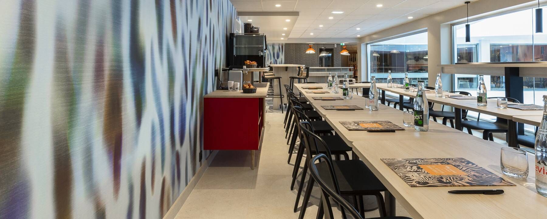 A modern dining area with long tables, black chairs, and a red counter.