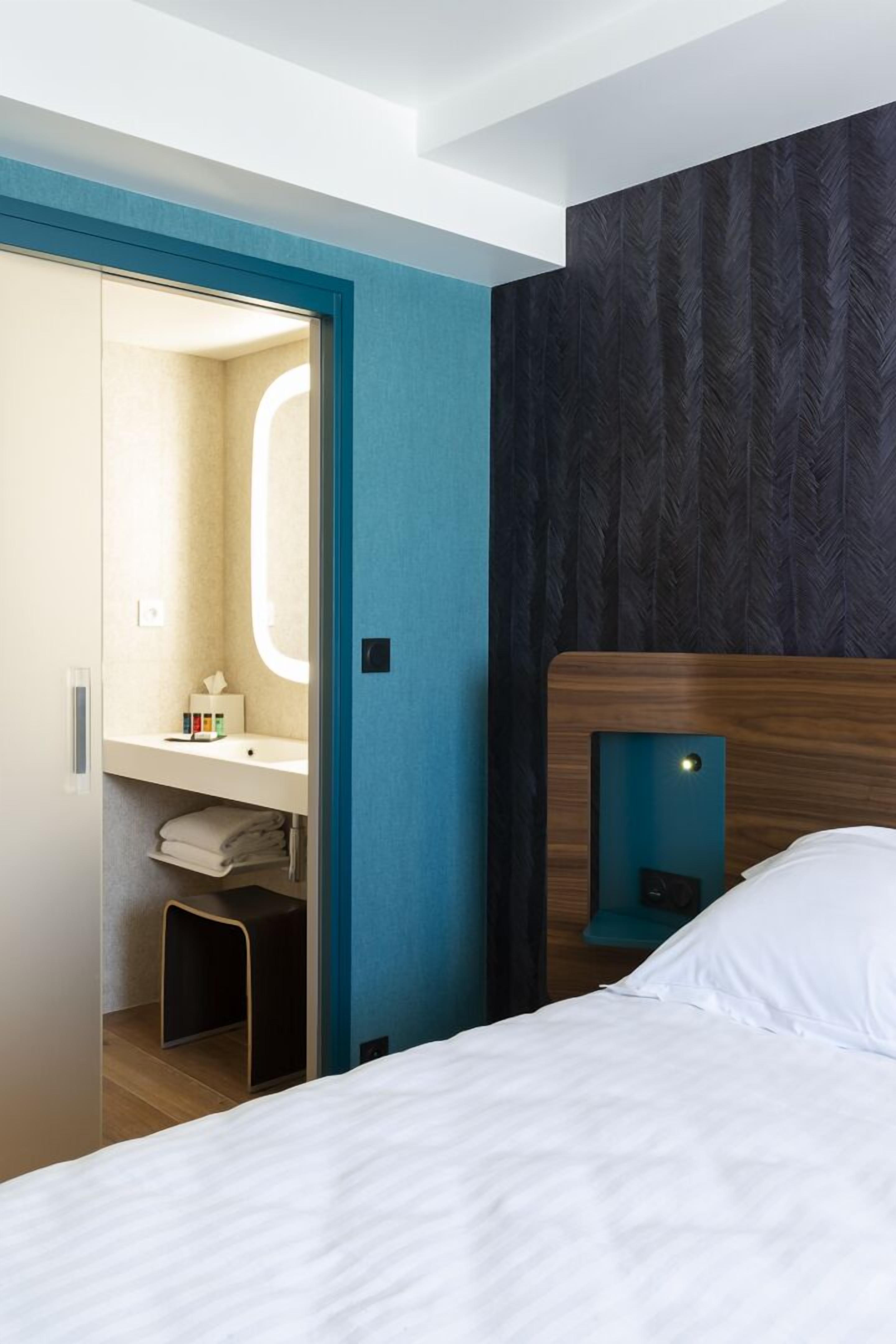 A hotel room with a bed, a nightstand, a bedside table, a mirror, and a wardrobe.