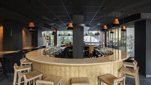 Zona de bar moderna con una barra curva, taburetes de madera y lámparas colgantes.
