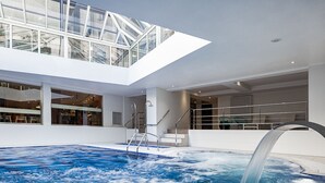 Una piscina interior moderna con techo de cristal, agua cristalina y zona de jacuzzi.