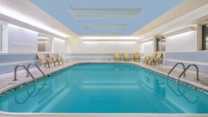 Una piscina interior con agua azul cristalina, rodeada de sillones de descanso y un suelo de baldosas.