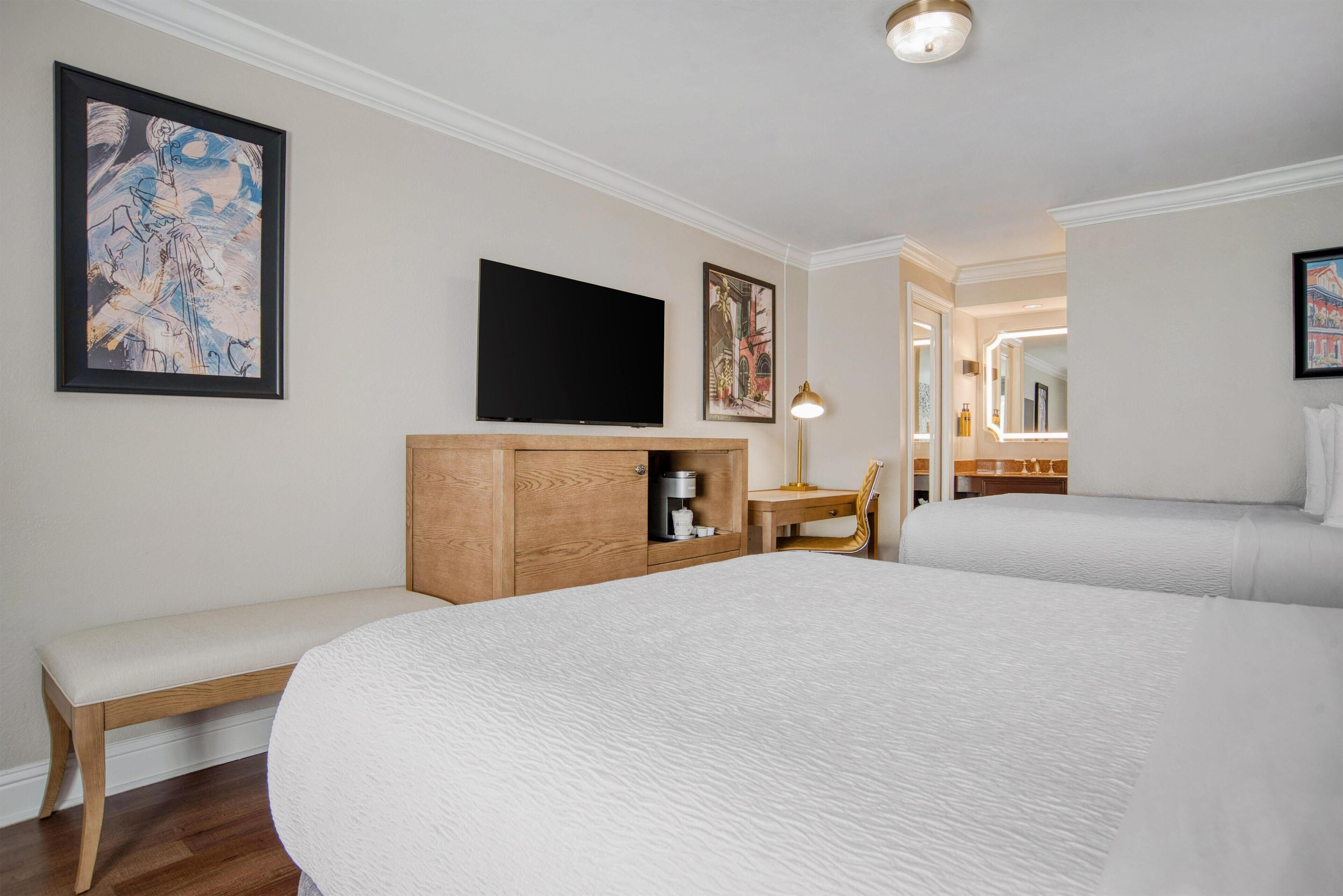 Une chambre d’hôtel avec un grand lit, un banc en bois, un bureau avec une lampe, une télévision et des œuvres d’art accrochées aux murs.
