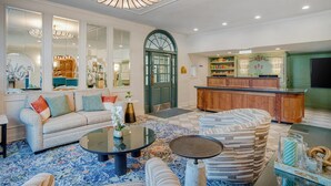 A spacious living area with a sofa, coffee table, and patterned rug. A green door and wooden cabinets are visible in the background.