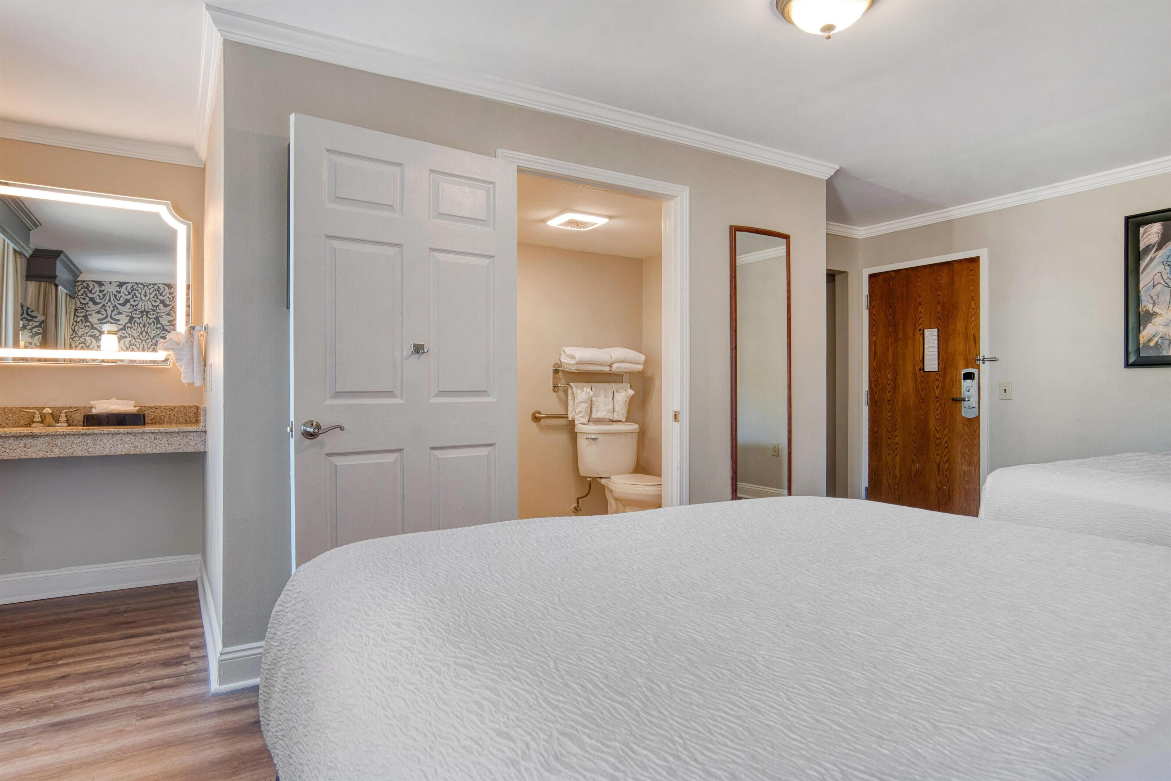 Une chambre d’hôtel avec un grand lit, une salle de bain avec des toilettes et un porte-serviettes, et une porte en bois.