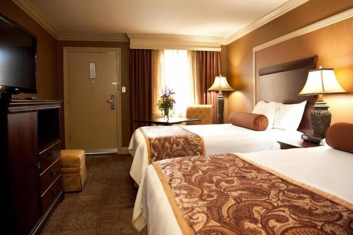 A hotel room with two beds, a TV, a desk, and a chair.