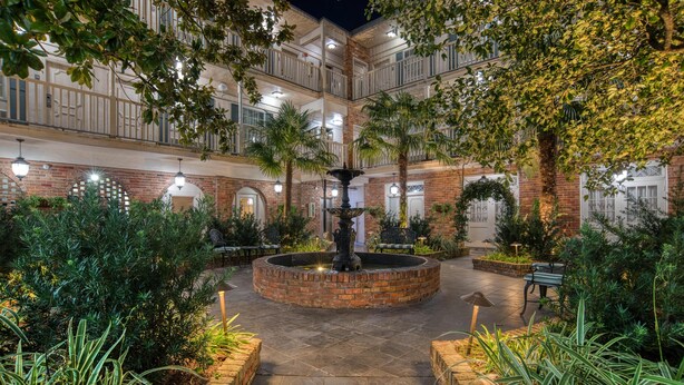 A courtyard with a central fountain, surrounded by brick walls and greenery.