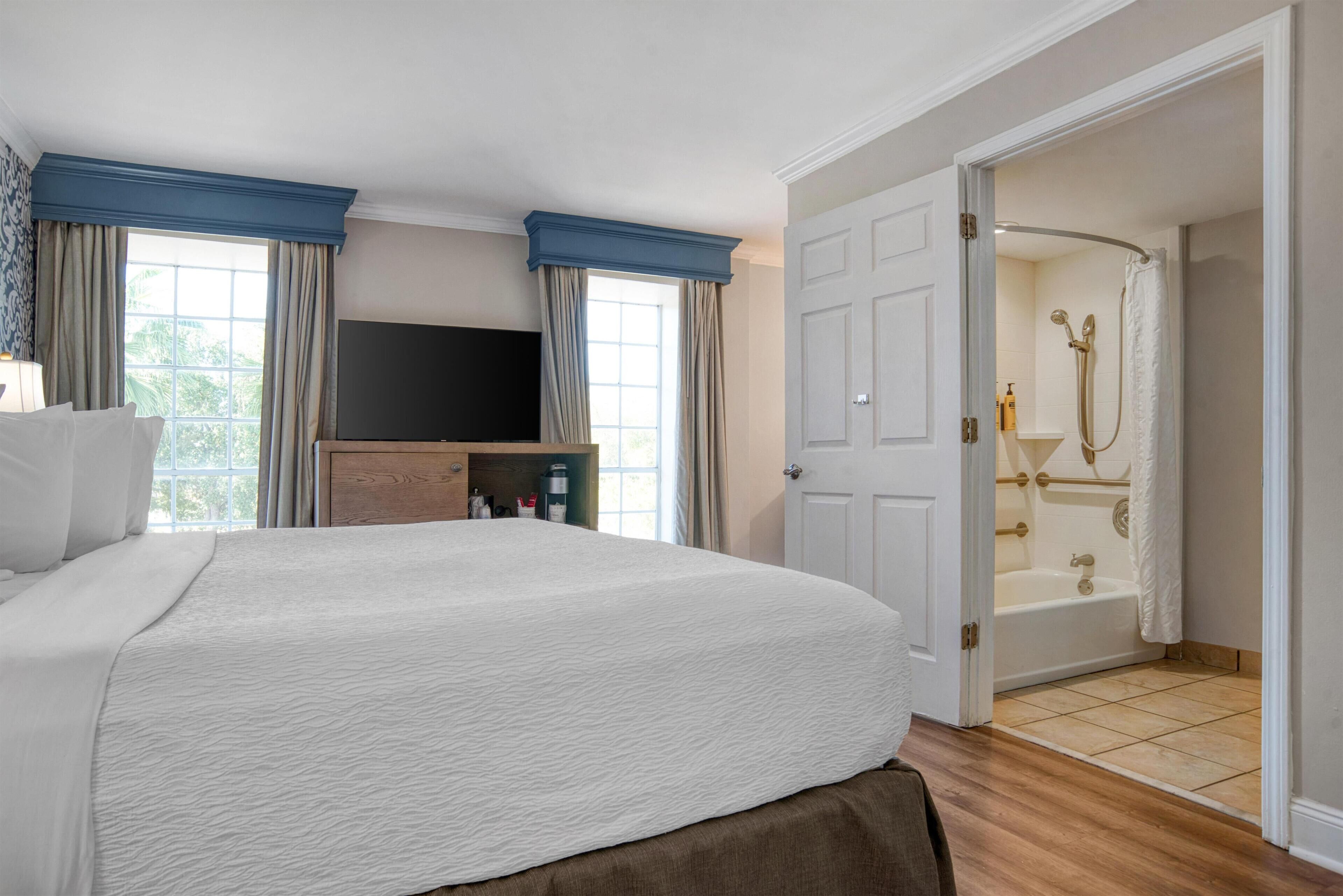 A hotel room with a large bed, a TV, a wooden cabinet, and a bathroom with a bathtub and shower.