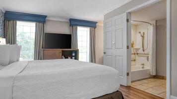 A hotel room with a large bed, a TV, a wooden cabinet, and a bathroom with a bathtub and shower.