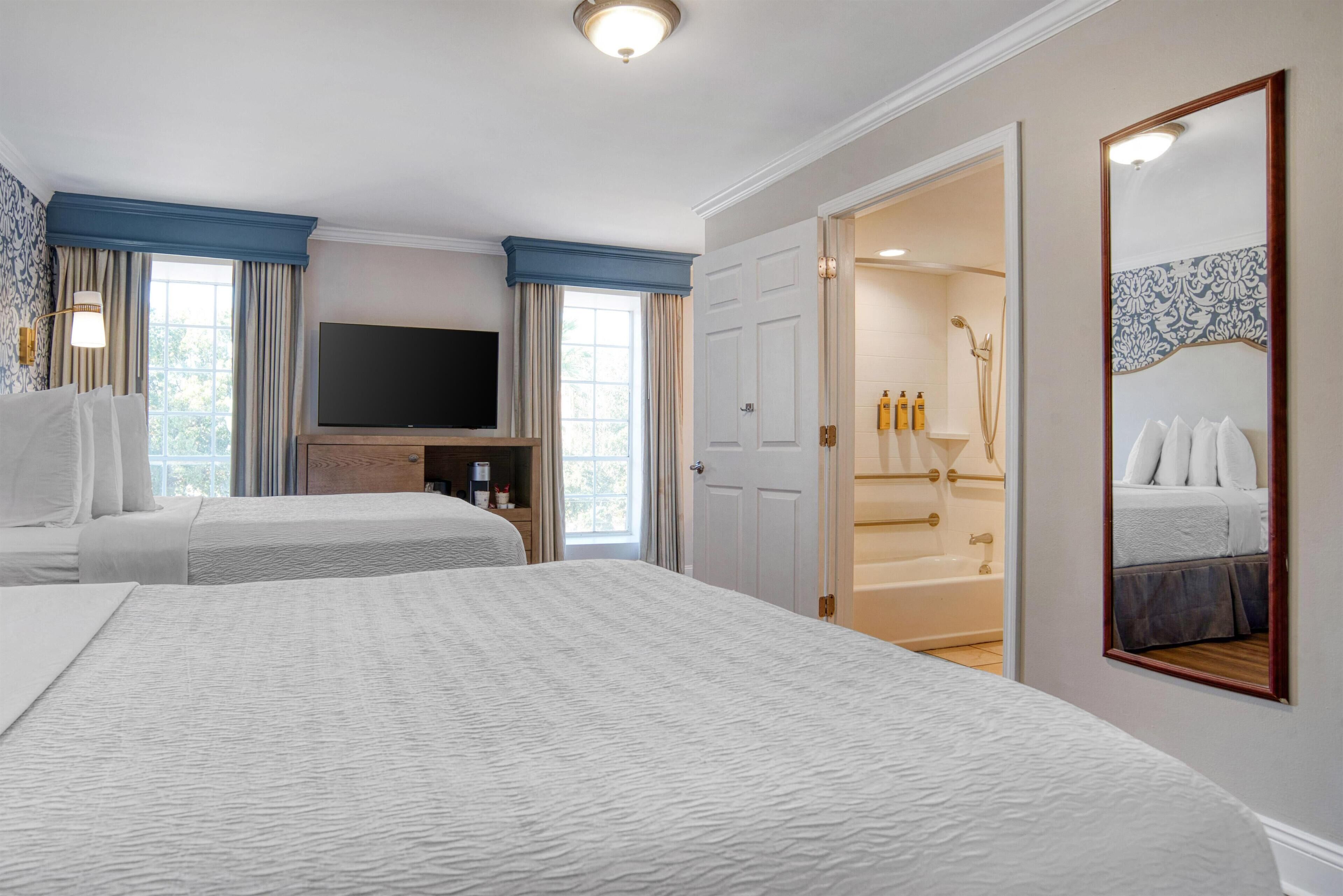 A hotel room with two beds, a TV, a bathroom with a bathtub, and a large mirror.