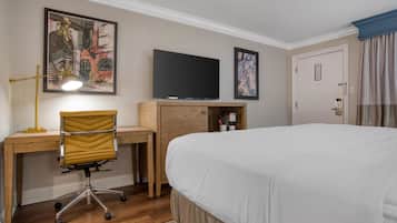 Une chambre d’hôtel équipée d’un lit, d’un bureau, d’une chaise, d’une télévision et ornée d’œuvres d’art sur les murs.