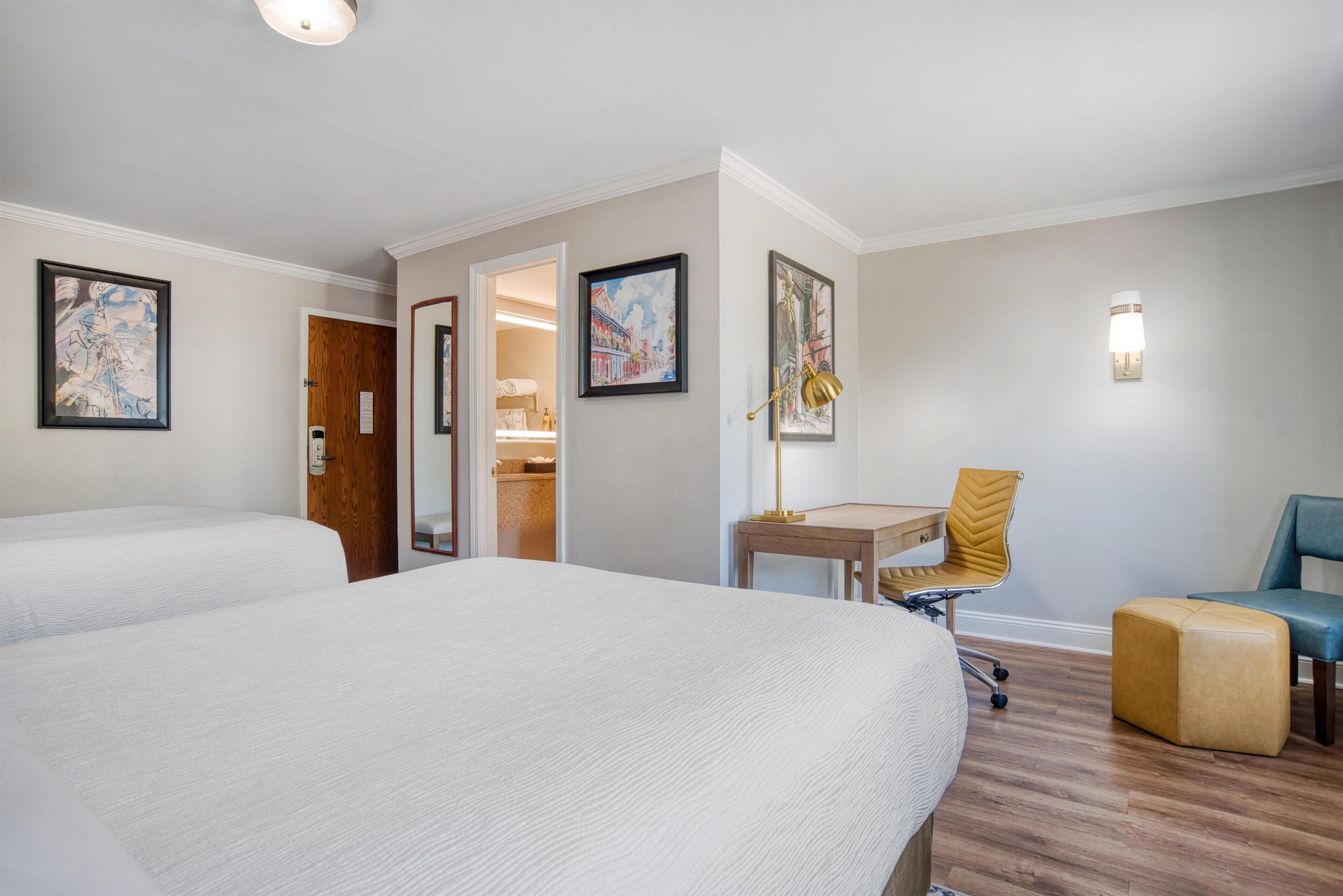 Habitación de hotel con dos camas, un escritorio, una silla y un pequeño reposapiés.