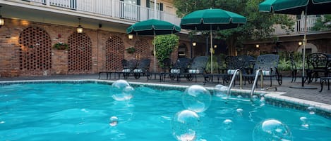 A swimming pool with bubbles, surrounded by outdoor seating and umbrellas.