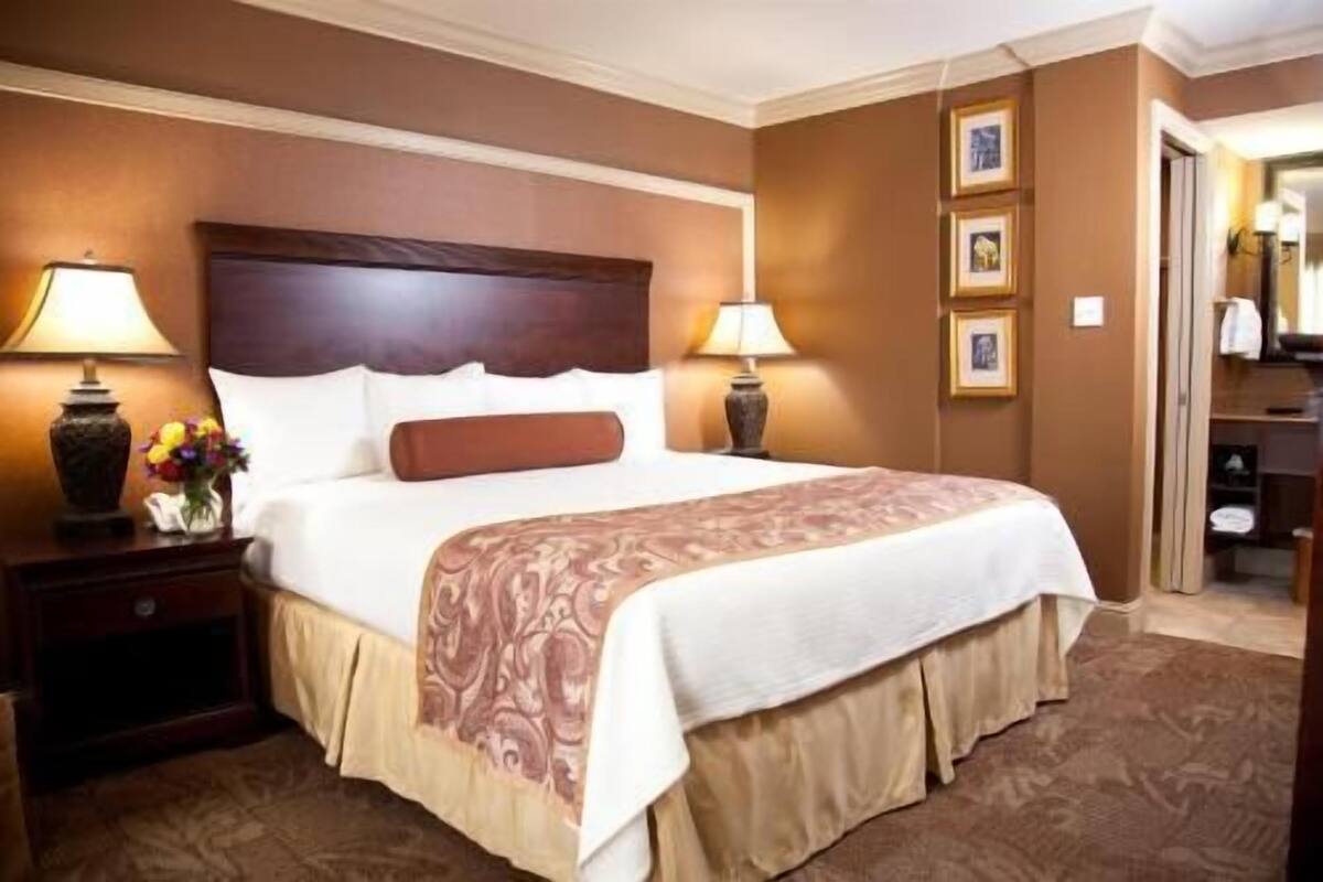 A hotel room with a large bed, two bedside tables with lamps, a nightstand, and a dresser.