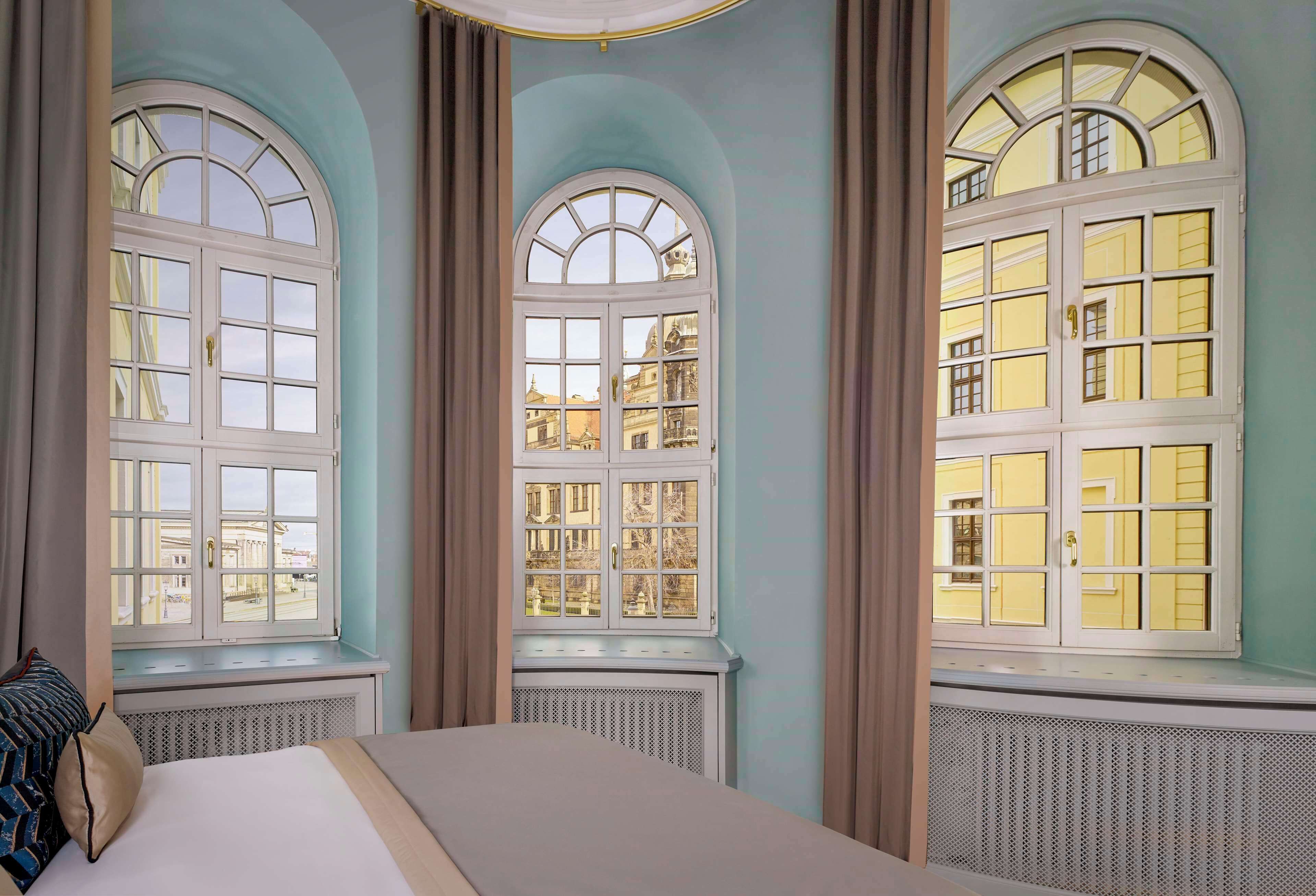A hotel room with three large arched windows, a bed, and a radiator.