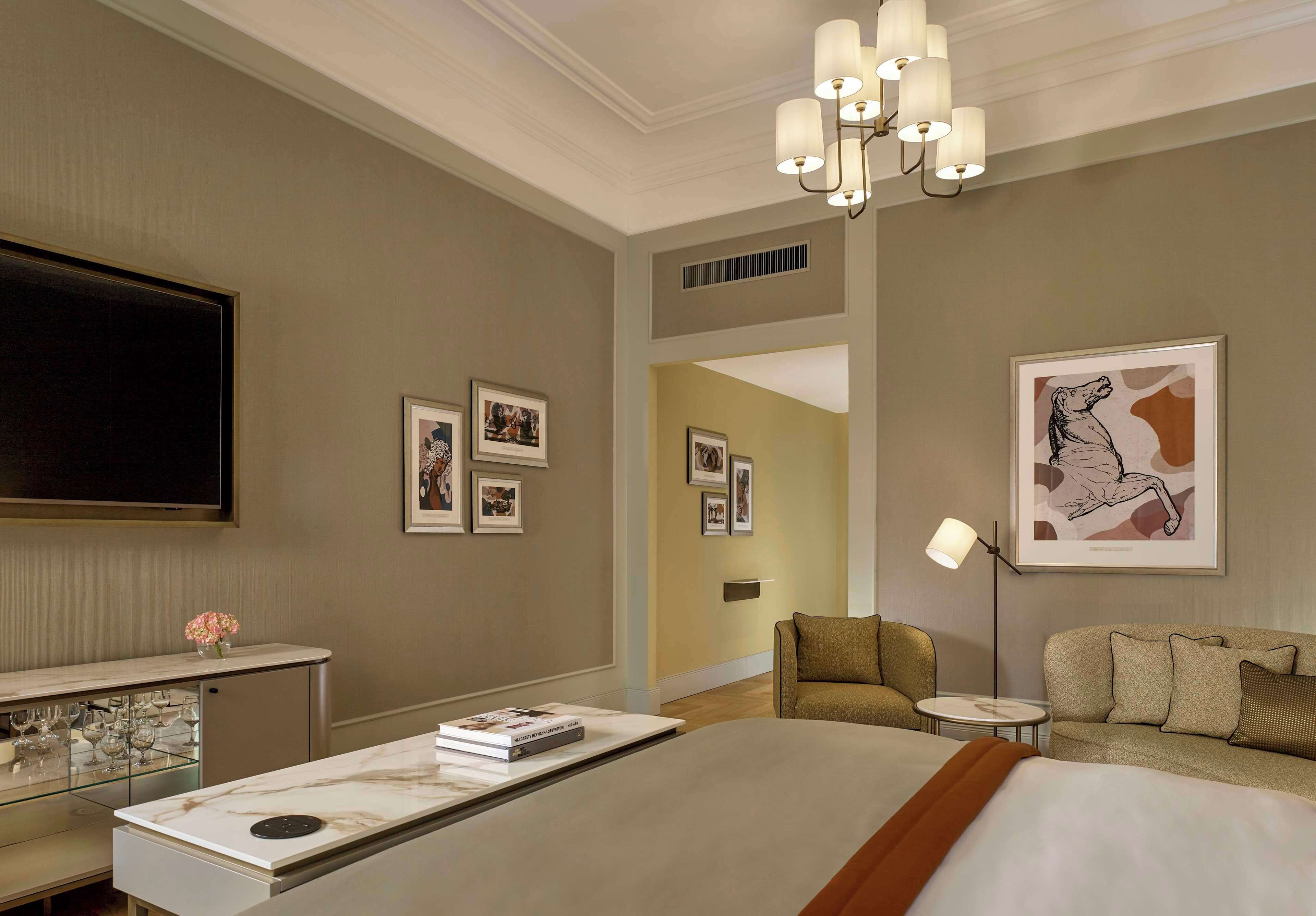 A hotel room with a large bed, a desk with a lamp, a sofa, and artwork on the walls.