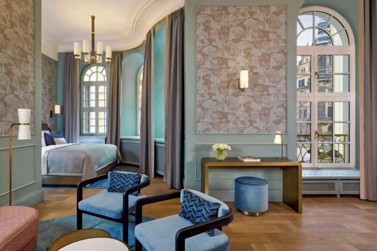 Ein Hotelzimmer mit einem Bett, zwei Stühlen, einem kleinen Tisch, einer Bank und einem Fenster mit Blick.