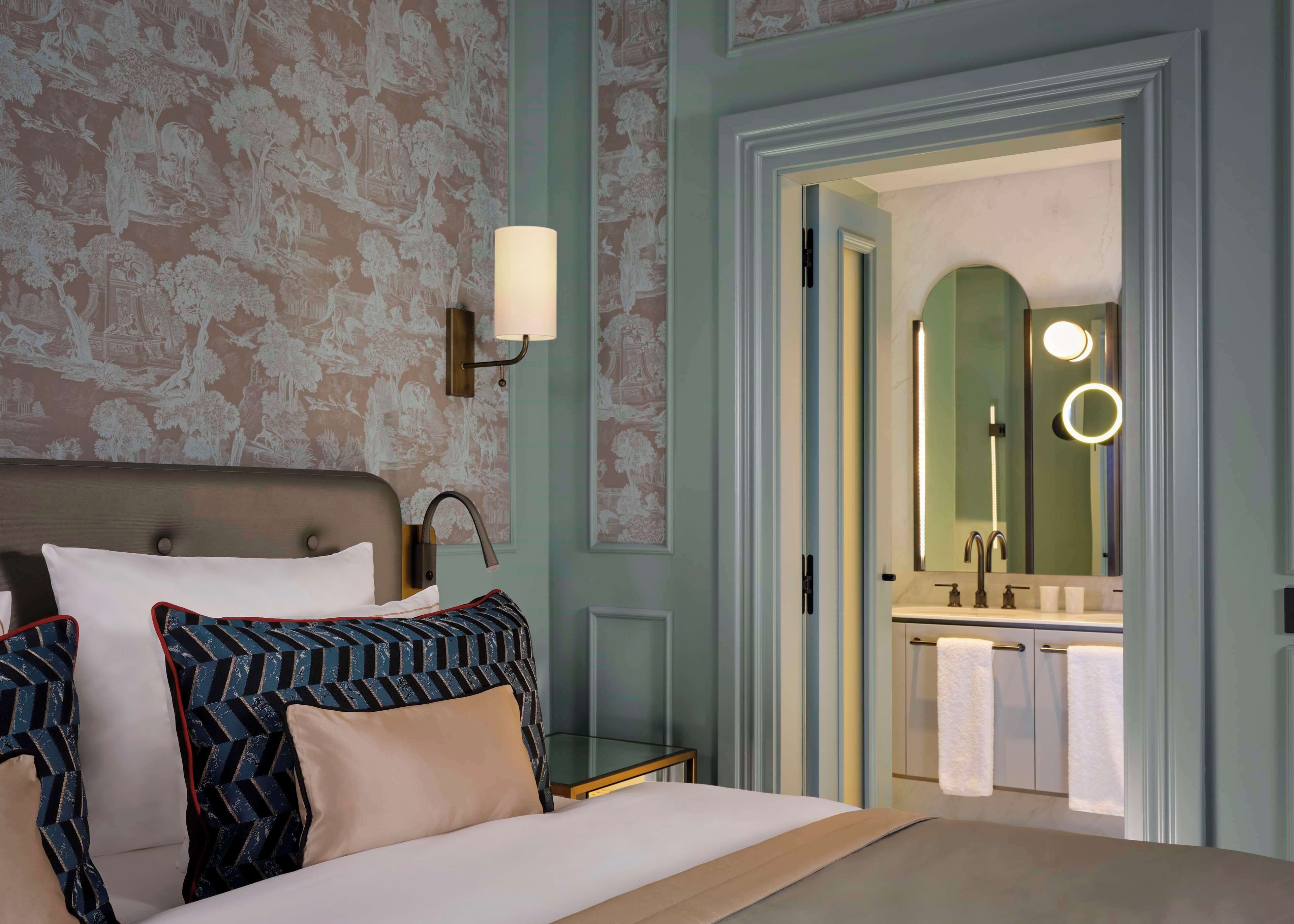 Een hotelkamer met een bed, een nachtkastje, een wandlamp en een badkamer die door een open deur zichtbaar is.