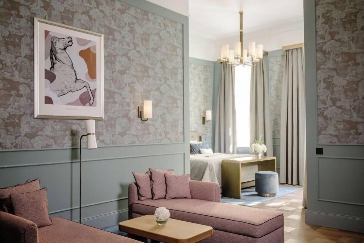 Ein Hotelzimmer mit einer Couch, einem kleinen Tisch, einem Bett, einem Nachttisch, einem Spiegel und einer Deckenleuchte.