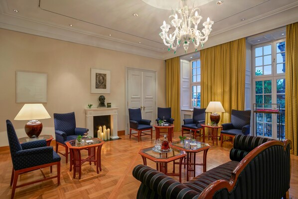 A well-lit room with a fireplace, multiple seating arrangements, and large windows with curtains.