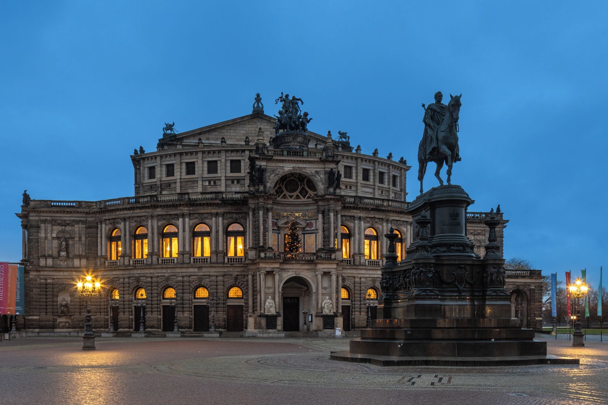 A historic building with classical architecture, featuring a central statue and a fountain in the foreground.