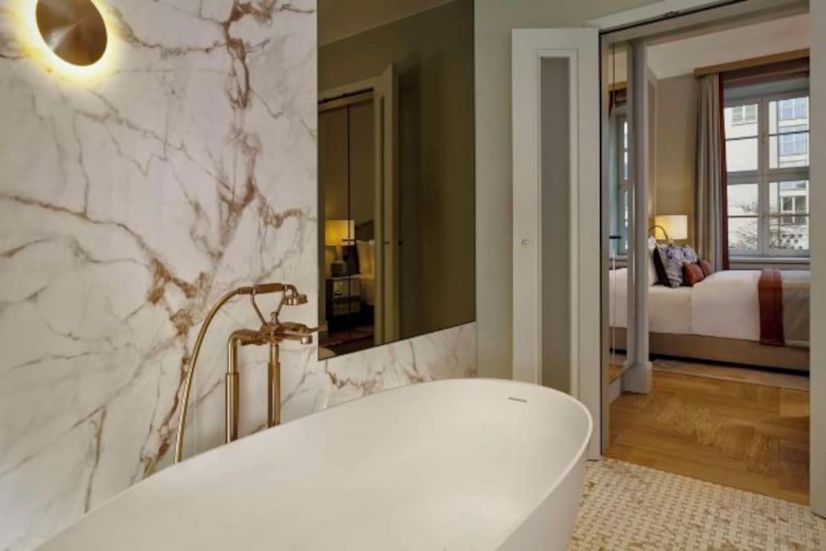Un baño moderno con pared de mármol, una bañera independiente y un espejo grande.