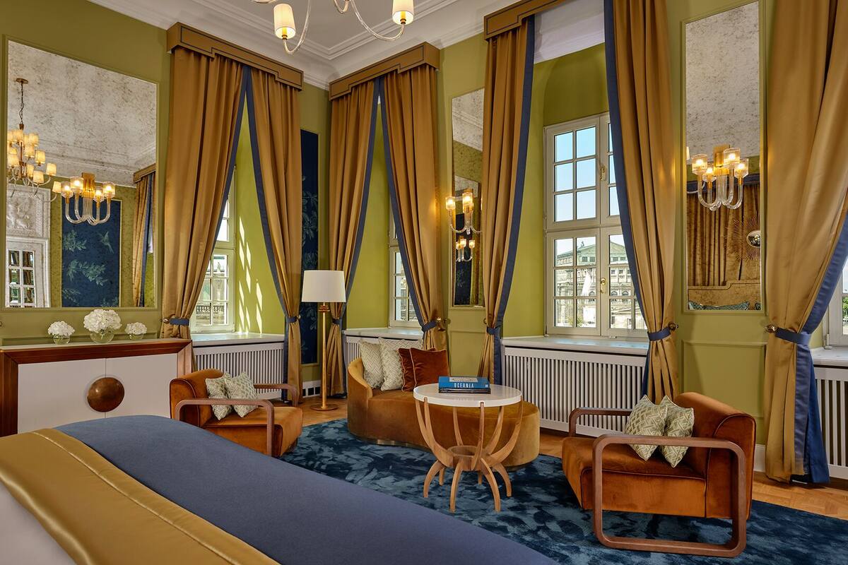 Ein Hotelzimmer mit einem großen Bett, zwei Sesseln, einem kleinen Tisch und einem Fenster mit Vorhängen.