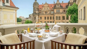 Een balkon met een ontbijttafel, met uitzicht op een historisch pand met versierde architectuur.