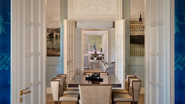 Une salle à manger élégante, avec une longue table, des chaises et une vue sur le paysage urbain, visible à travers une porte ouverte.