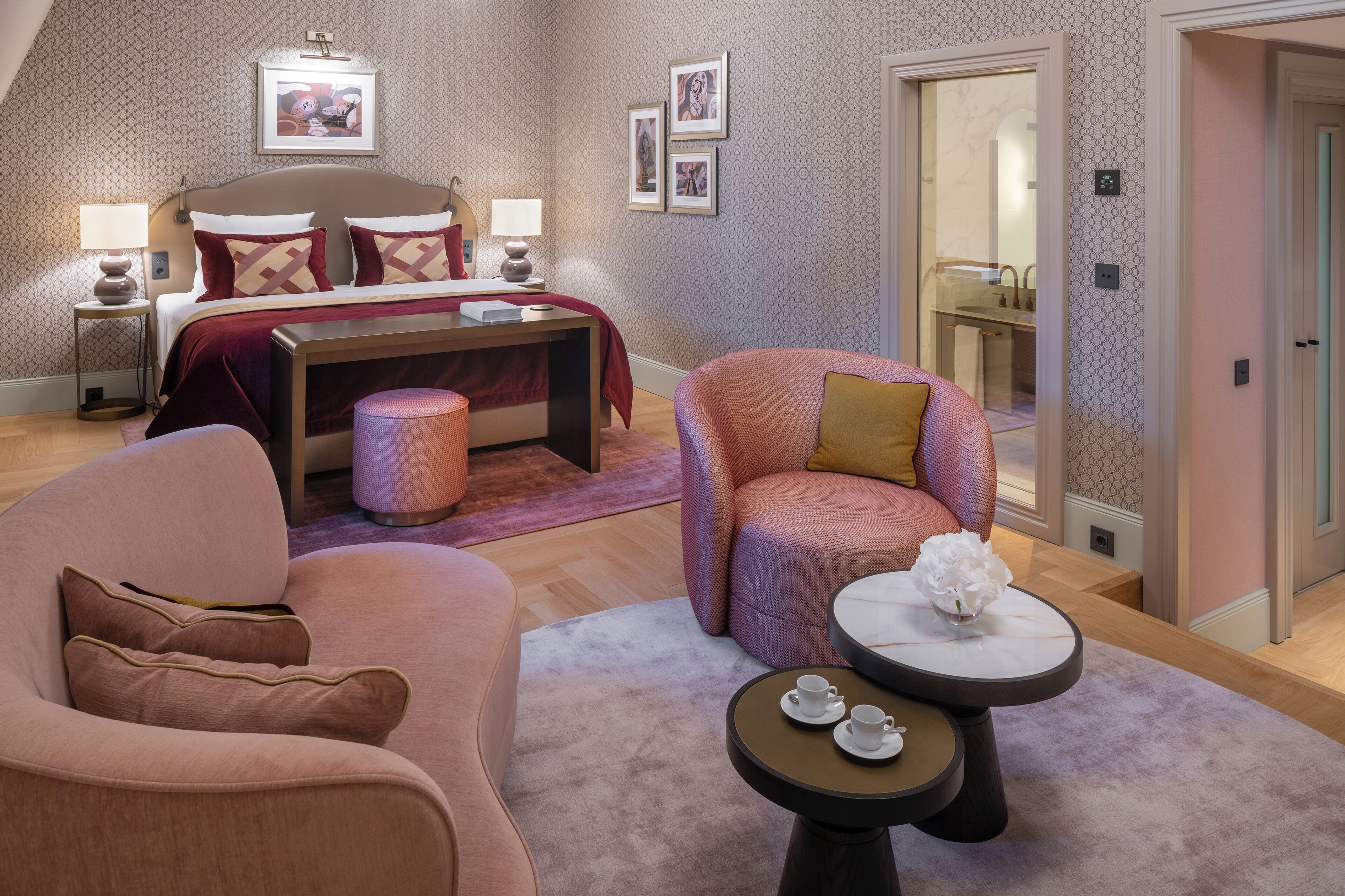 Une chambre à coucher comprenant un lit, des tables de chevet, une commode, une chaise, une table ronde et un petit tabouret.