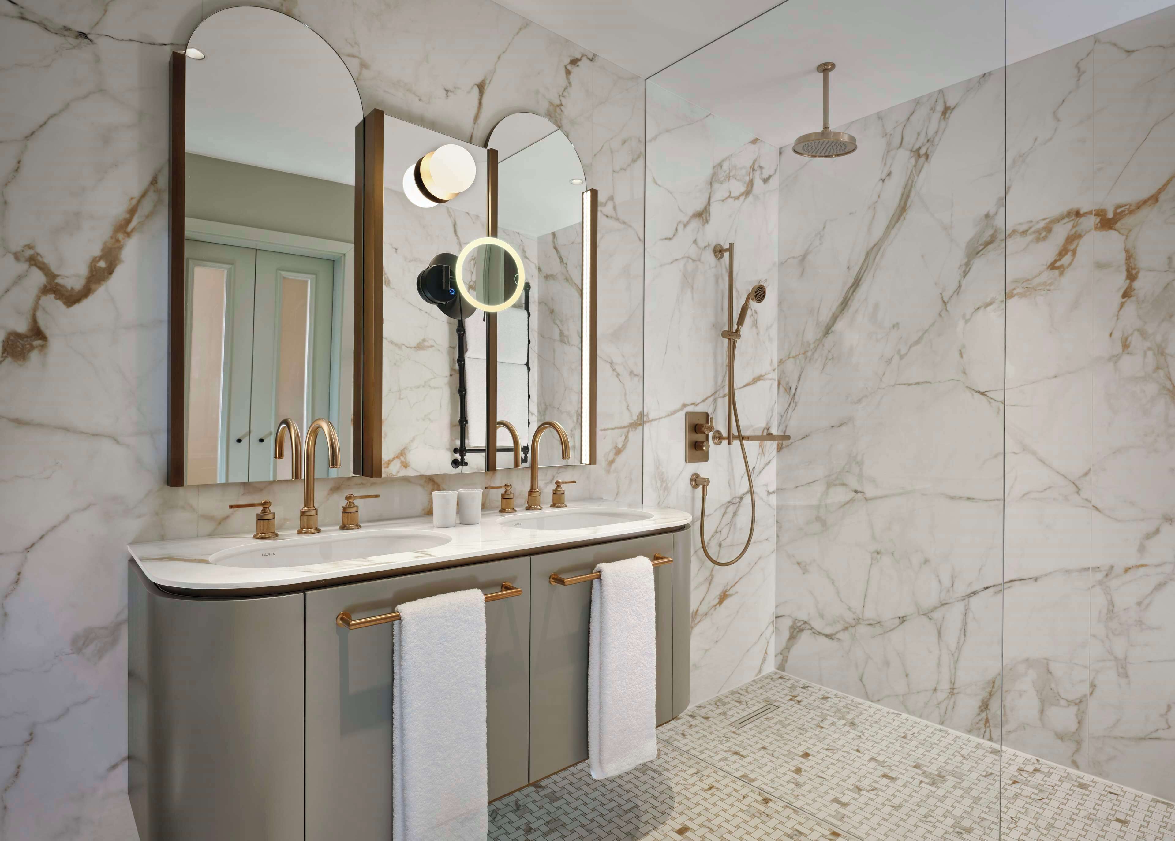 Un baño moderno con pared de mármol, un espejo grande, dos lavamanos y una ducha.