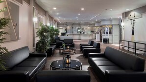 Un moderno hall de hotel con sofás de cuero negro, mesas redondas y plantas en macetas.